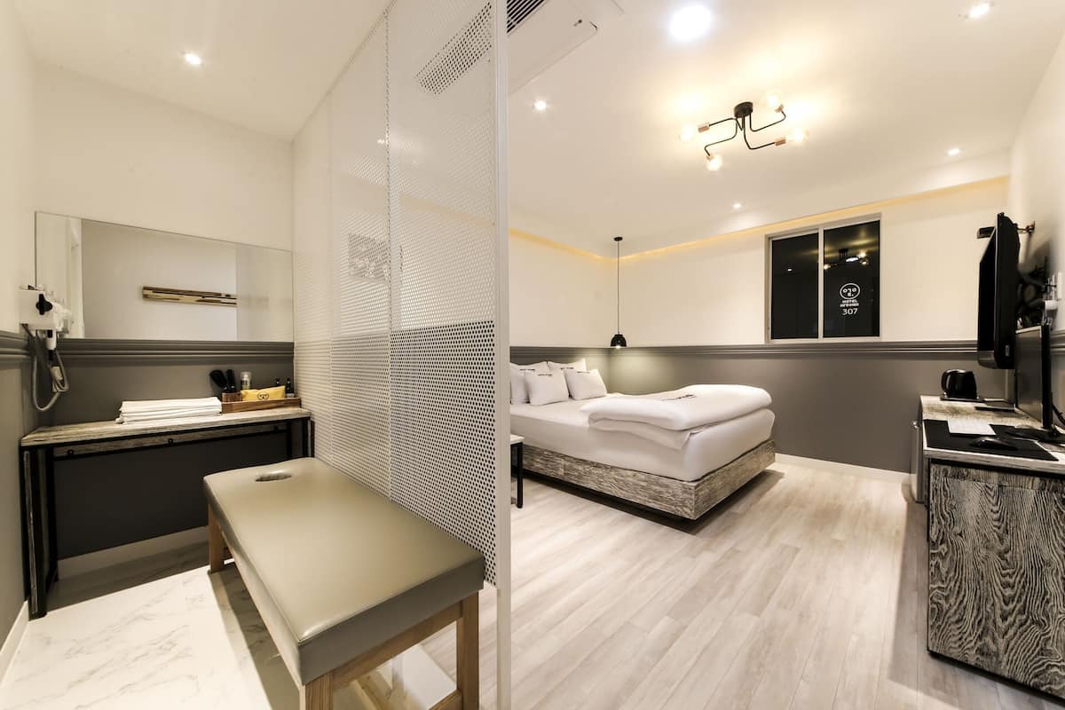 A modern hotel room with a bed, bedside table, and a desk with a chair.