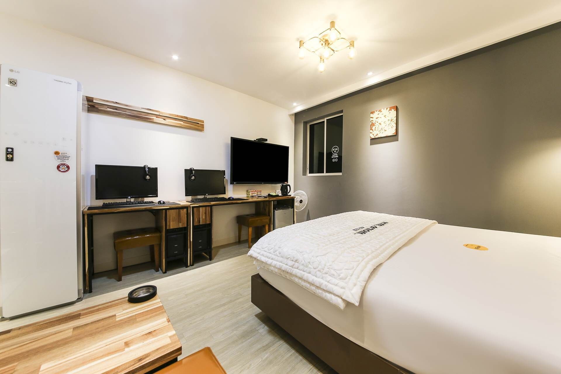 Una habitación de hotel moderna con una cama, dos escritorios con computadoras, un televisor y un minibar.