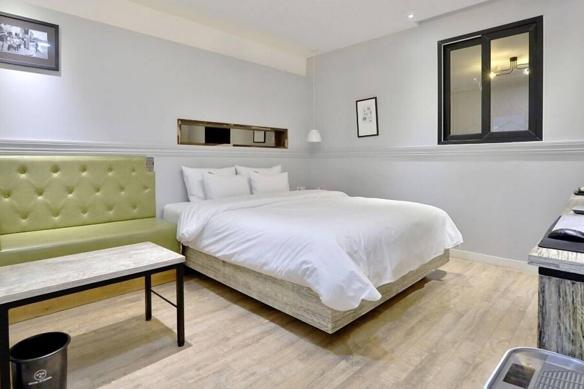 A hotel room with a bed, a green sofa, a small table, and a trash bin.