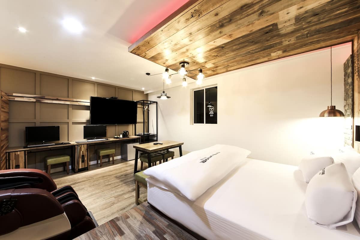 A modern hotel room with a wooden ceiling, a bed, a desk, a TV, and a dining area.