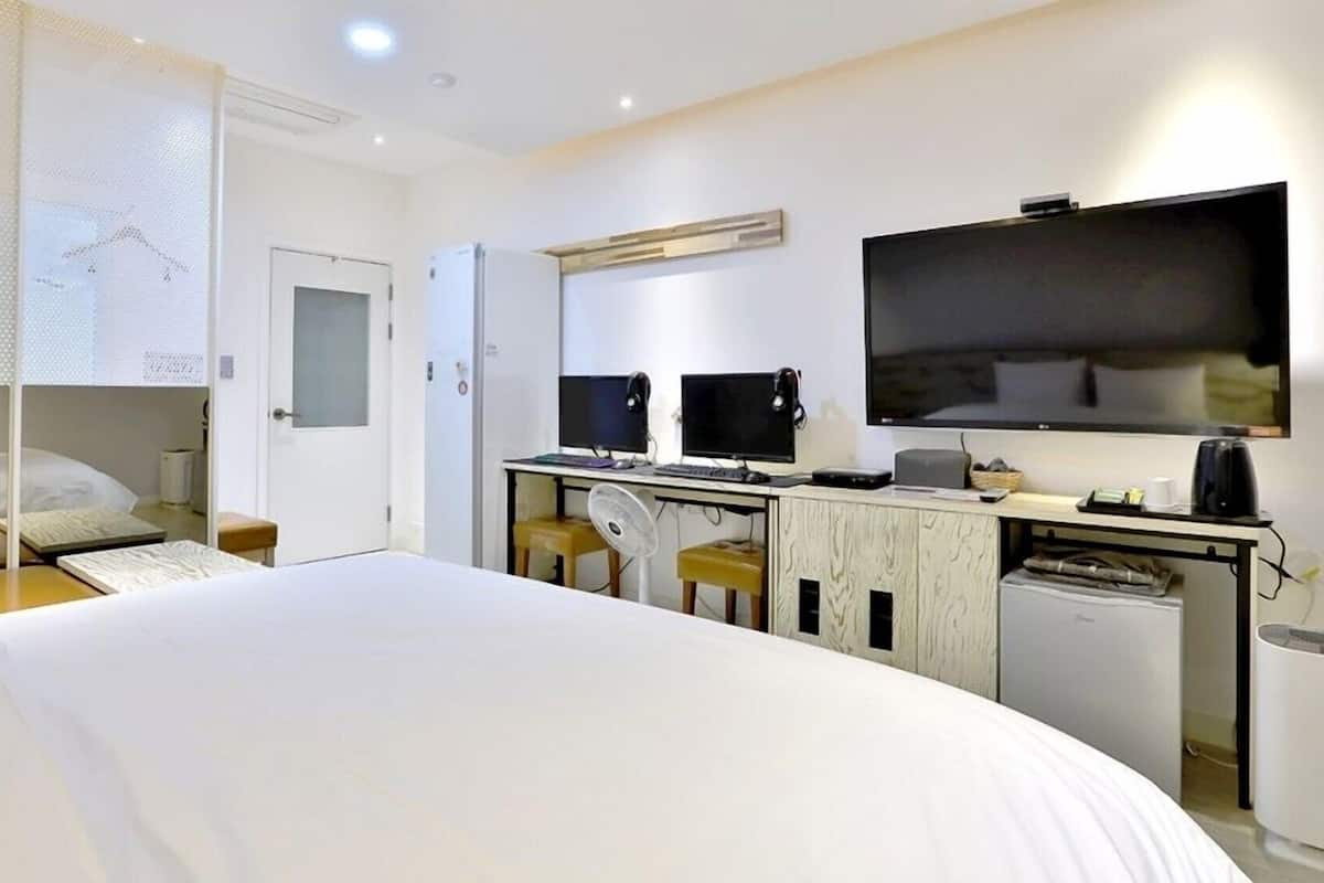 A hotel room with a bed, a desk with two monitors, a television, and a coffee machine.