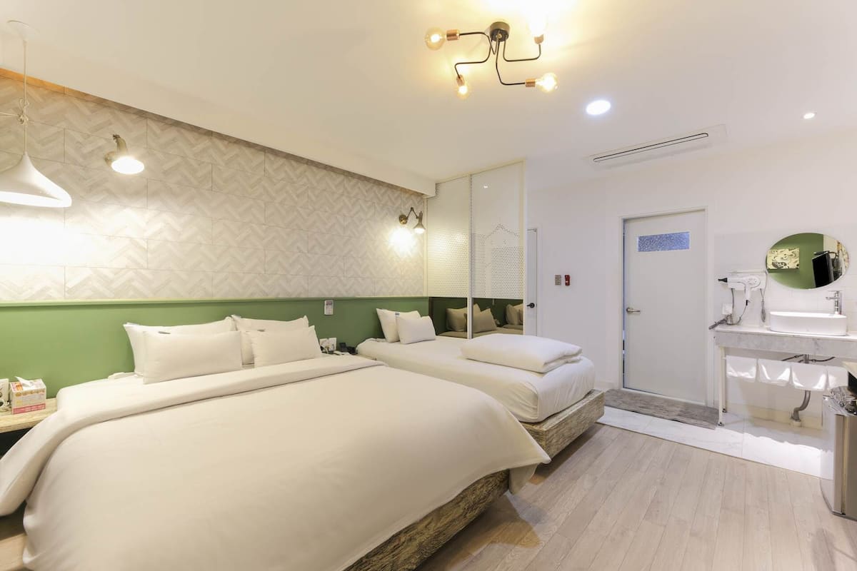 A hotel room with two beds, a bathroom with a sink and mirror, and a ceiling light fixture.