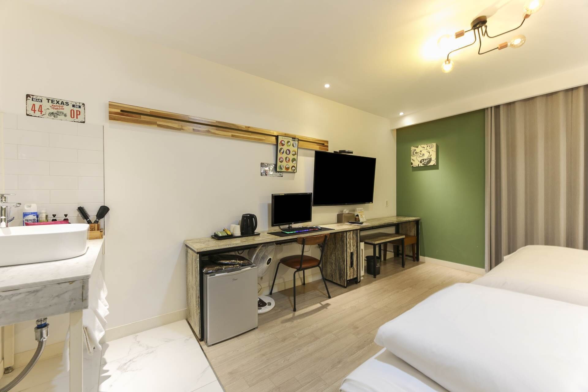 A hotel room with a bed, a desk with a computer, a television, and a small refrigerator.