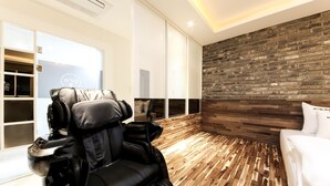 A modern room with a massage chair, a wooden floor, a brick wall, and a white bed. - The Stay Series (Daegu)