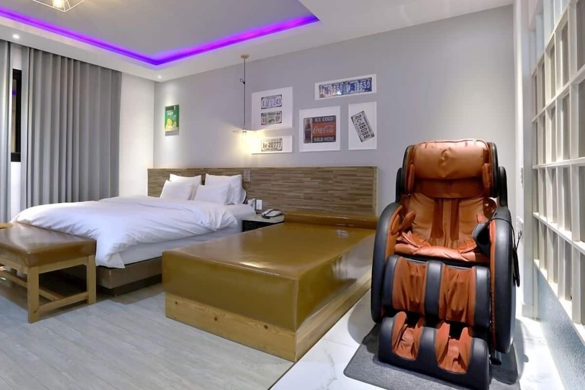 A hotel room with a bed, a massage chair, a wooden bench, and a small table.
