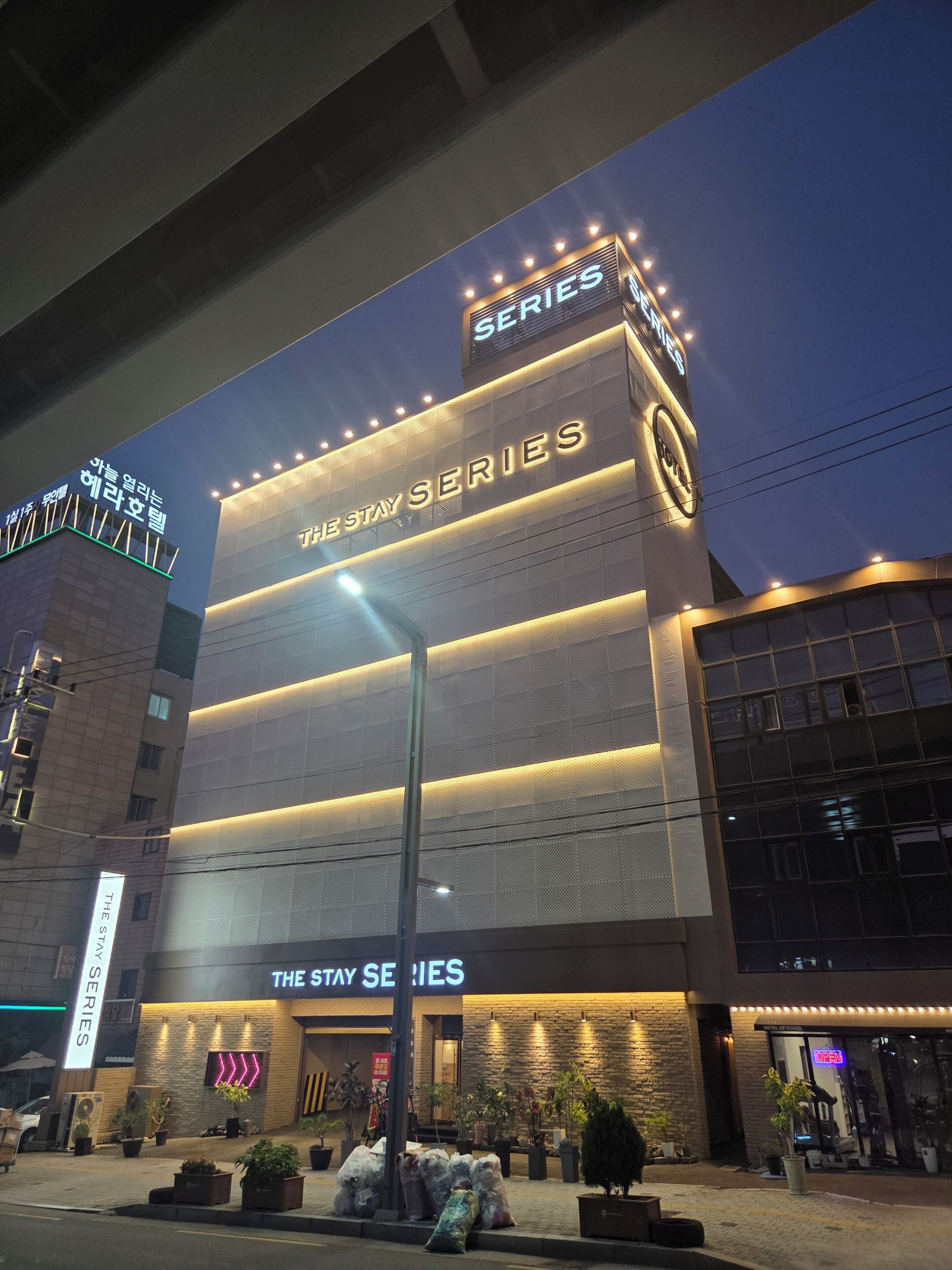 Un hôtel doté d'une enseigne bien visible sur laquelle on peut lire « THE STAY SERIES » et qui présente une architecture moderne.