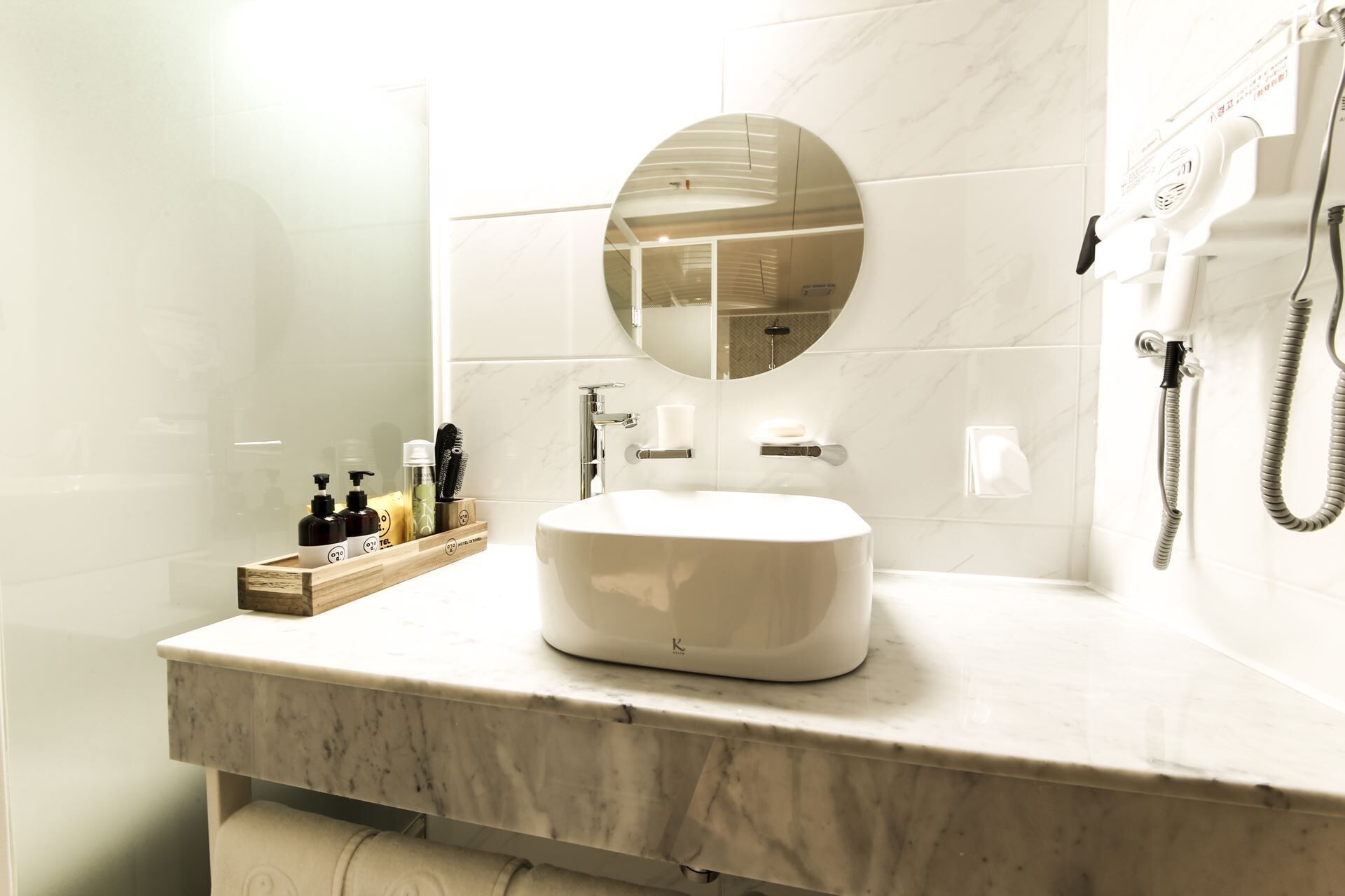 Un baño moderno con encimera de mármol, espejo redondo, lavabo blanco y cabezal de ducha de mano.