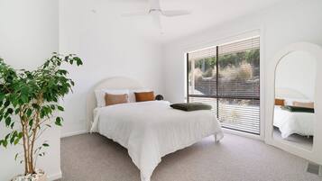 A bedroom with a bed, a ceiling fan, a window with blinds, a potted plant, and a mirror.