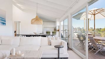 A modern living room with a white sofa, a round coffee table, and a dining area with a table and chairs.
