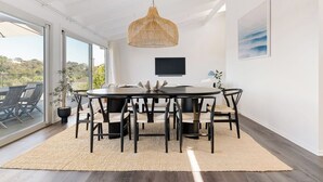 Un coin repas avec une table ronde, des chaises noires, un luminaire suspendu en fibres tressées, un téléviseur à écran plat et une vue dégagée grâce à de grandes fenêtres.