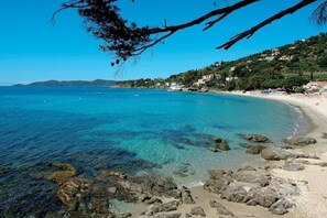 A coastal beach with clear waters, rocky shoreline, and buildings on a hillside. - Beautiful garden level with terrace, sea view and direct access to the beach - swimming pool (Bormes-les-Mimosas)