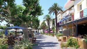 Een zonnig terras met tafels, stoelen, plantenpotten en parasols.