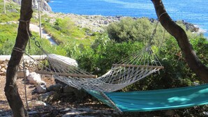 Una hamaca atada entre árboles con vistas a una costa rocosa y una vista despejada del mar.