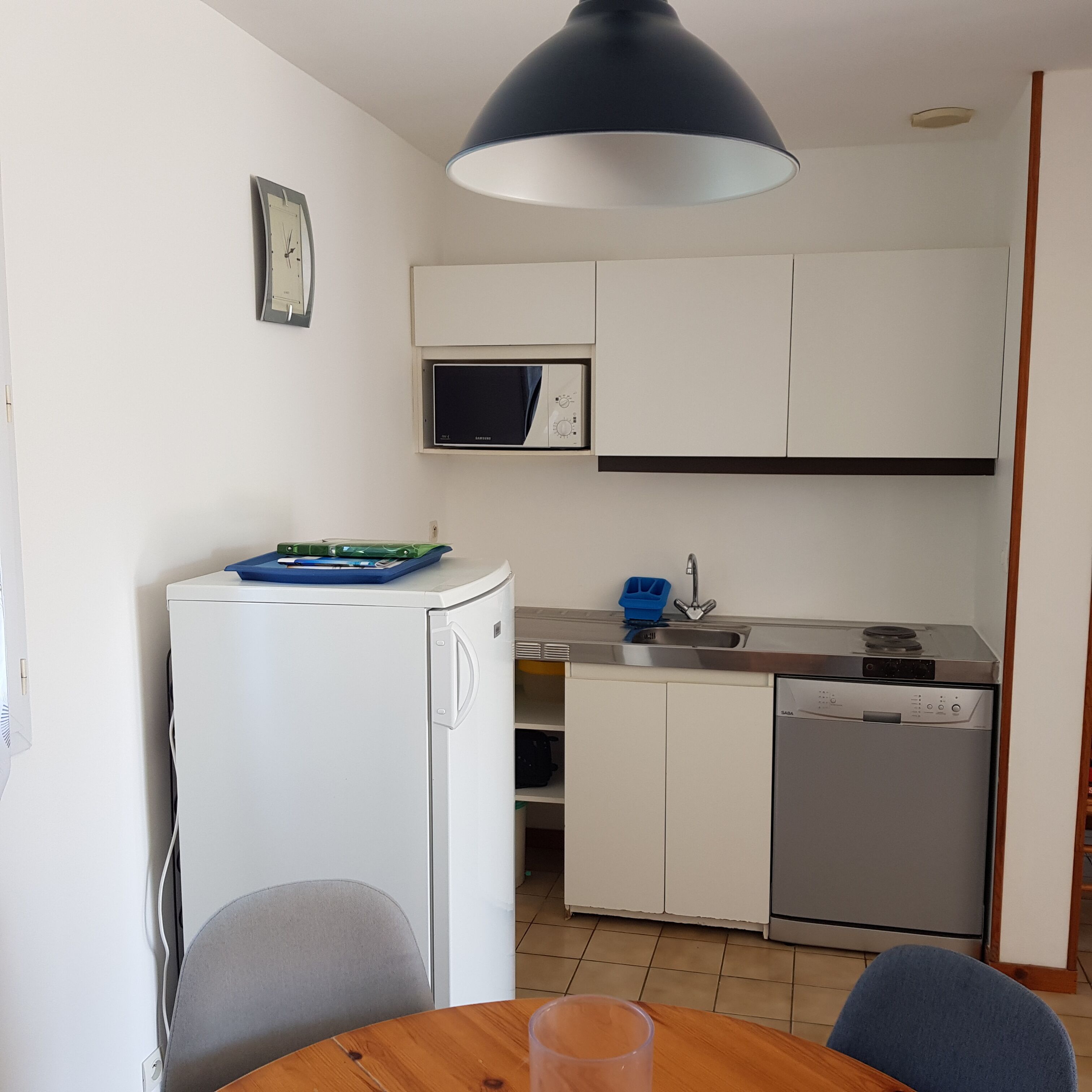 Een kleine keuken met witte kastjes, een magnetron, een vaatwasser en een koelkast.