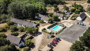 Oversigtsbillede af en kystresort med flere hytter, en swimmingpool og en tennisbane.