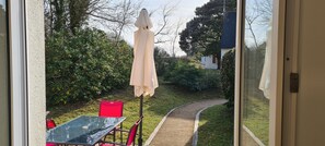 A view through a glass door of a patio area with a table, chairs, and a white umbrella. - Comfortable House with a Pool in Morbihan, Southern Brittany (Erdeven)