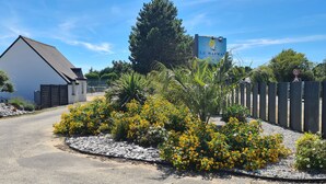 Et boligområde med et hvidt hus, en have med hegn og gule blomster, samt et skilt med fartgrænse.