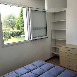 A bedroom with a bed, a dresser, a window with a view of greenery, and a shelf unit. - Comfortable House with a Pool in Morbihan, Southern Brittany (Erdeven)
