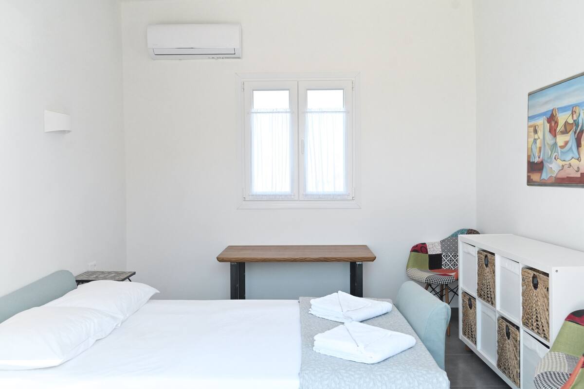 Une chambre à coucher avec un lit, une petite table, un banc, une armoire et une fenêtre.