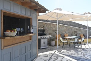 An outdoor patio with a grill, table, chairs, and umbrellas. - Dolce Vista (Paros)