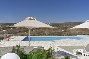 A pool area with lounge chairs and umbrellas, surrounded by a stone patio and a view of the countryside. - Dolce Vista (Paros)