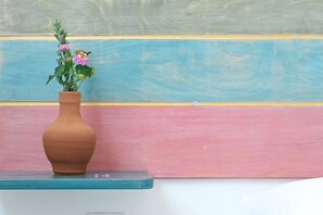 A terracotta vase with pink flowers on a teal shelf against a wall with horizontal stripes. - Dolce Vista (Paros)