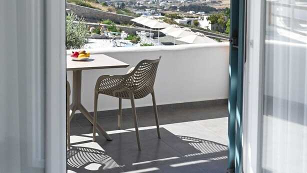 Un balcón con una pérgola de madera, una mesa con sillas y vistas a un pueblo costero.