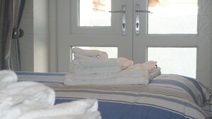 A bed with a striped blue and white bedspread, a stack of folded white towels, and a white door with a handle. - Luxury child and baby friendly rural retreat. Close to Porthleven and St Ives (Helston)