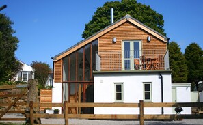 Une maison moderne dotée d’une grande baie vitrée, d’une terrasse en bois et d’une porte verte.