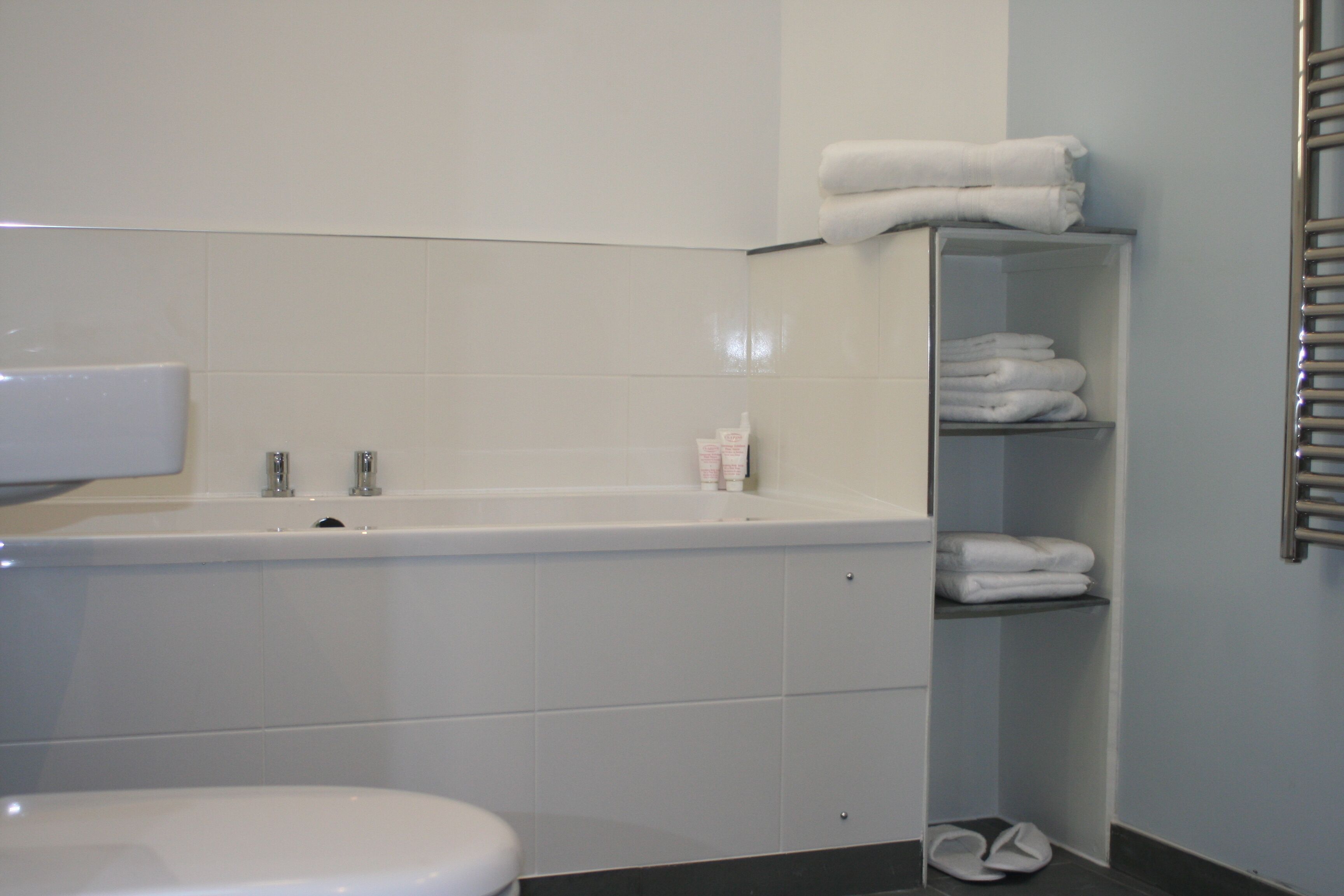 Une salle de bain avec une baignoire blanche, des toilettes et un porte-serviettes avec des serviettes pliées.