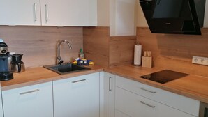 A modern kitchen with white cabinets, a stainless steel sink, a black stove, and wooden countertops. - App. Seeblick, Hanseatenhaus (Sylt)