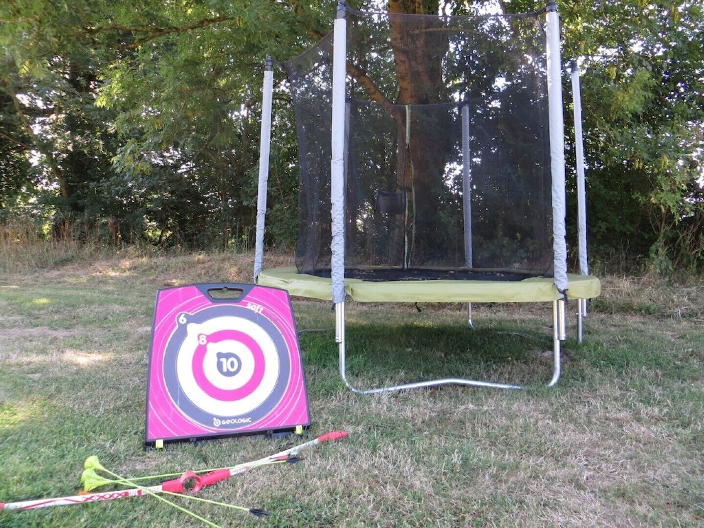 A trampoline with a net enclosure, a target board, and a slingshot on a grassy area.