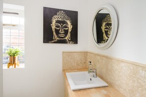 A bathroom with a white sink, a mirror, and a Buddha-themed artwork on the wall. - Detached Forest Setting Bungalow (Little Sampford)