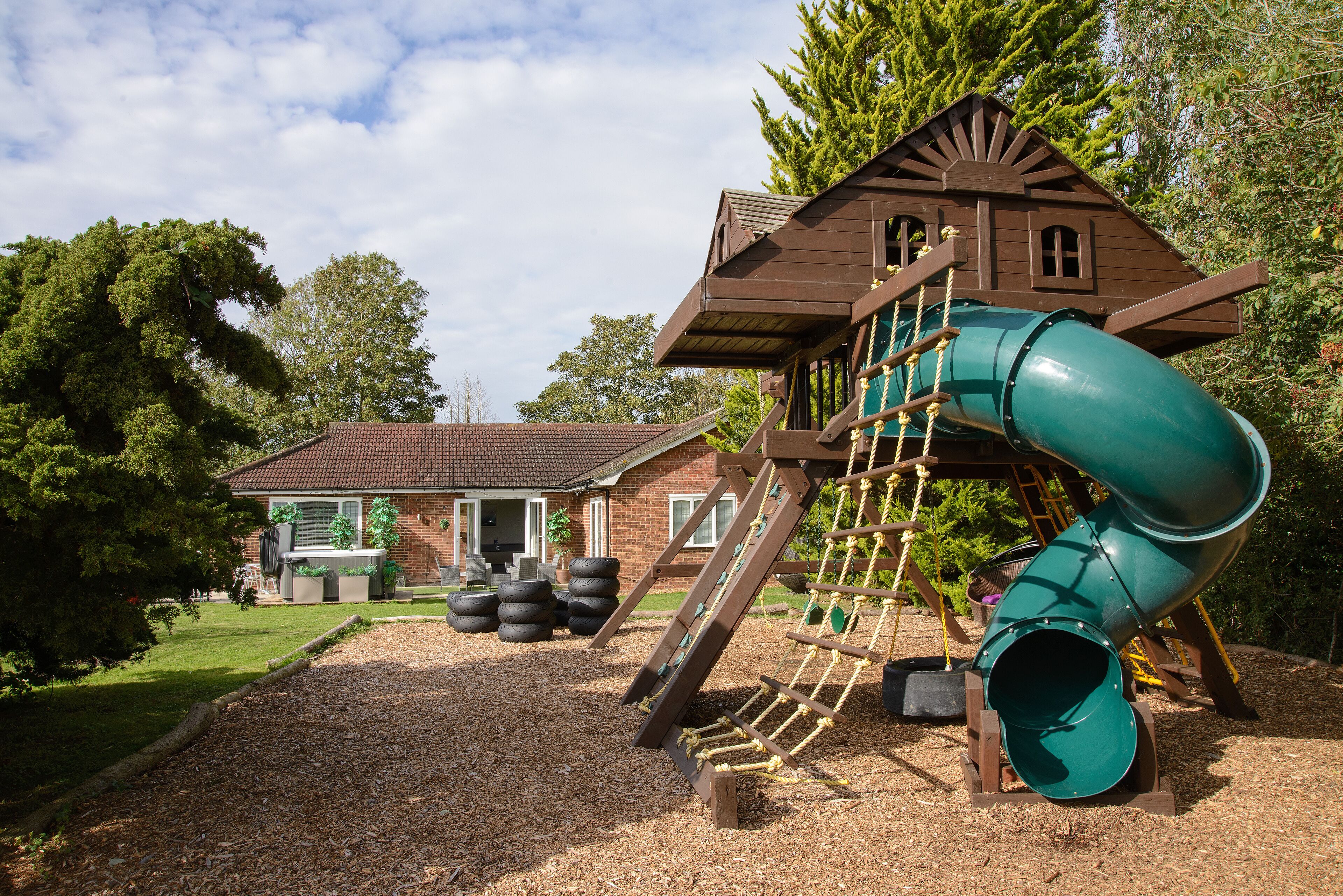 A playground with a slide, climbing net, and a wooden playhouse.