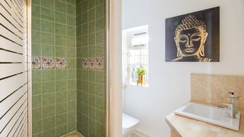 A bathroom with green tiled walls, a white sink, and a Buddha painting.