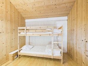 Une chambre avec des lits superposés, dont les murs et le plancher sont en bois.