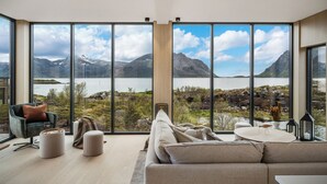 A modern living room with a large window offering a scenic mountain and lake view. - NEW! Luxury Cabin in beautiful Lofoten (Nordland)