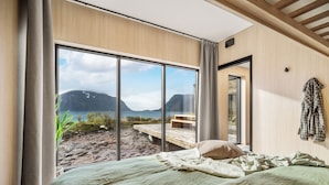 A bedroom with a large window offering a view of a beach and mountains. - NEW! Luxury Cabin in beautiful Lofoten (Nordland)
