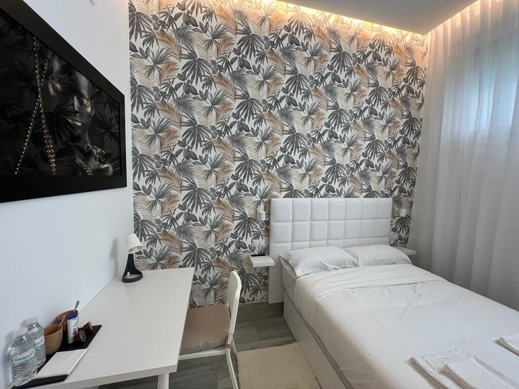 Ett sovrum med en vit säng, ett skrivbord med en stol och en vägg med ett tropiskt bladmotiv.