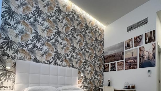 Una habitación de hotel moderna con una cama grande, un papel tapiz con estampado de hojas tropicales y varias fotografías de paisajes urbanos en la pared.
