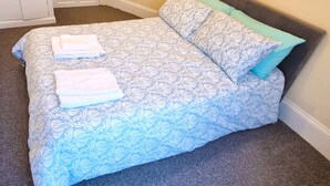 Un letto con copriletto e cuscini decorati, un asciugamano piegato e una porta sullo sfondo.