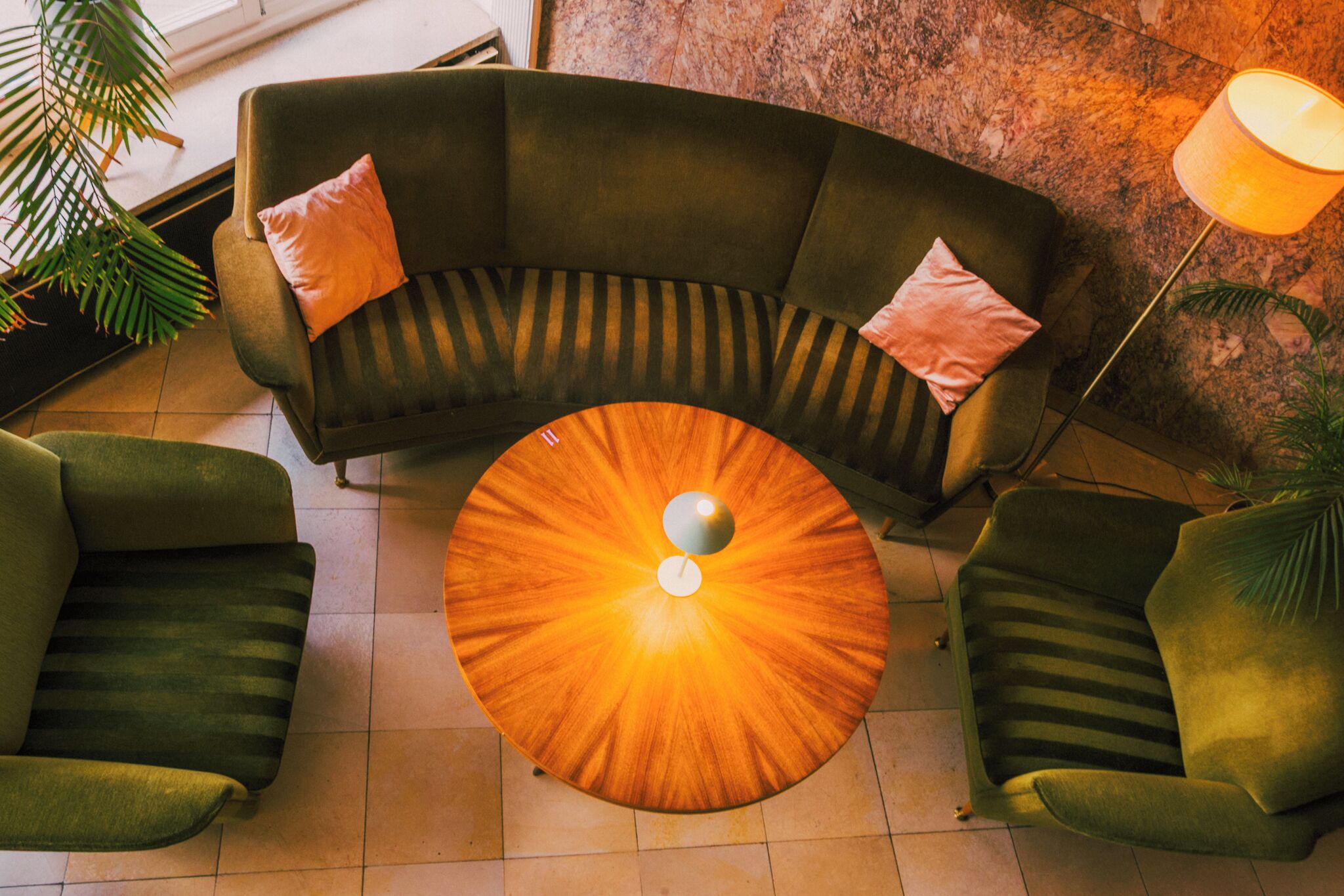A modern lounge area with a curved green sofa, two matching armchairs, and a round wooden coffee table with a central light fixture.