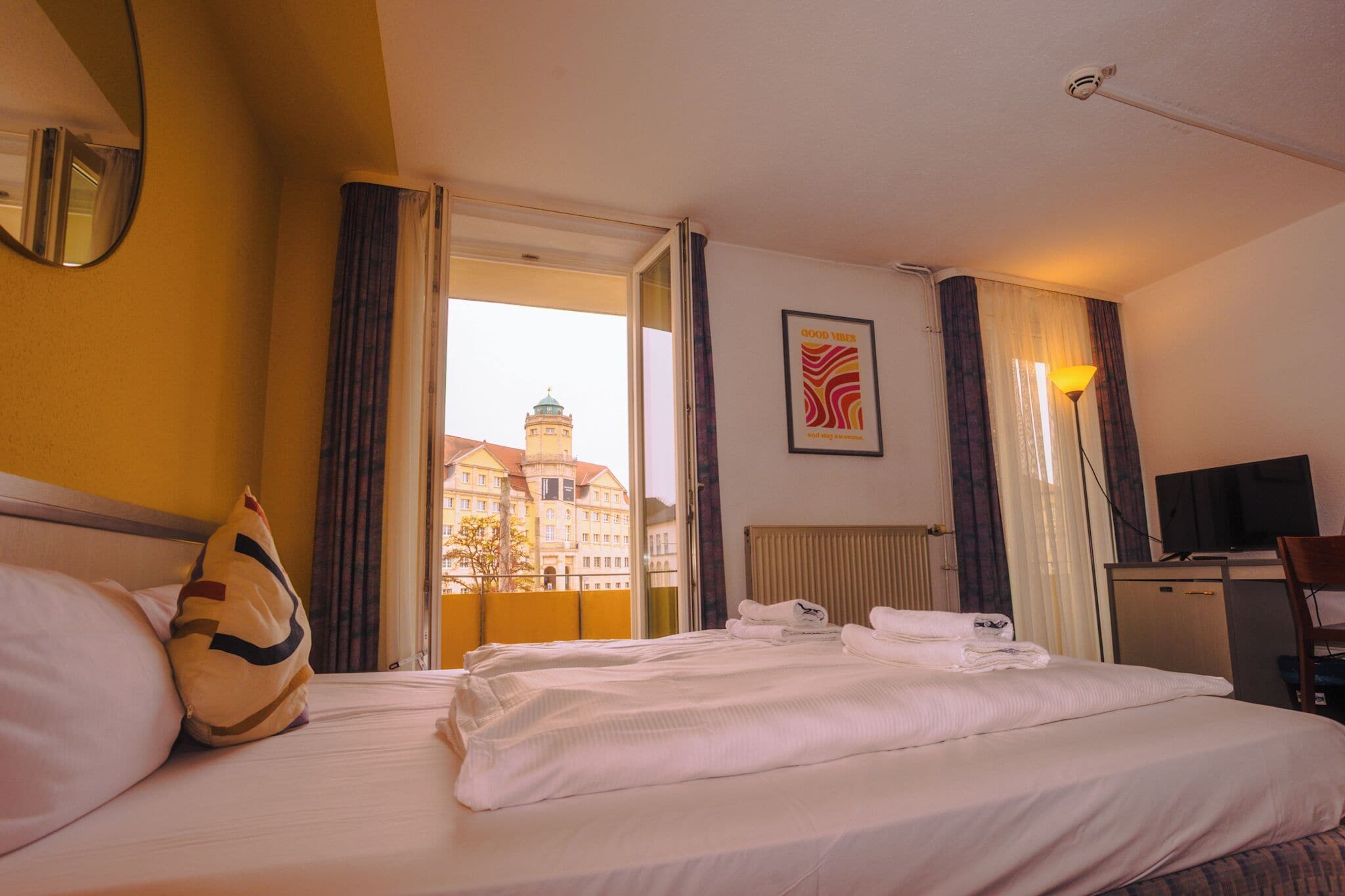 Una habitación de hotel con cama, escritorio, televisión y ventana con cortinas.