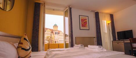 Una habitación de hotel con cama, escritorio, televisión y ventana con cortinas.