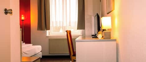 A hotel room with a bed, a desk with a lamp, a chair, and a window with curtains.