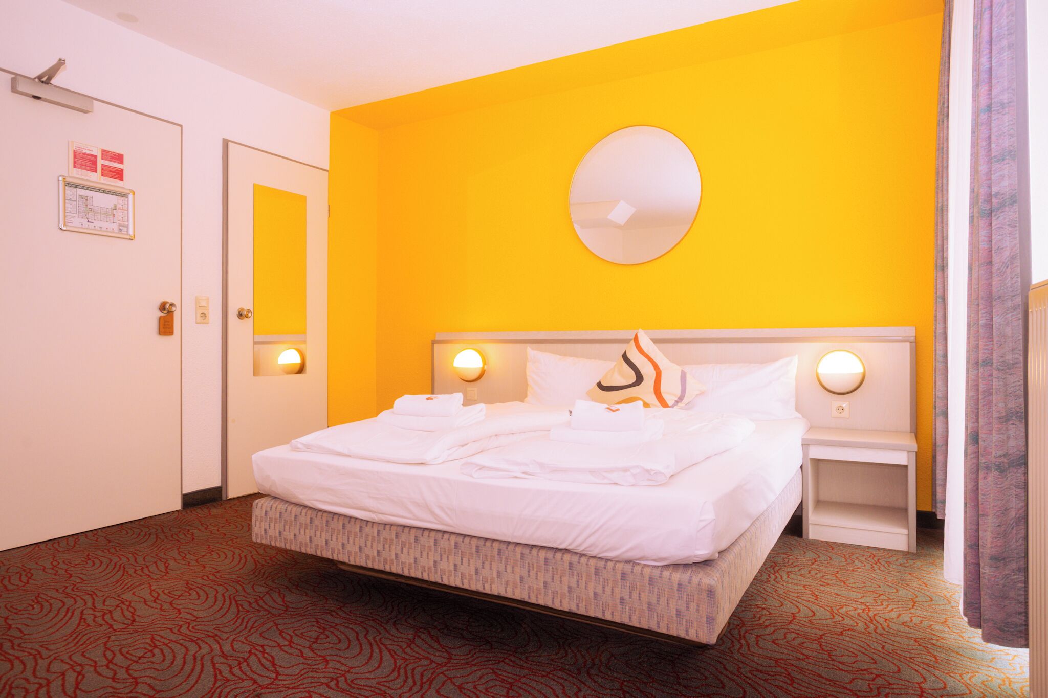 Una habitación de hotel con una cama, un espejo redondo y dos mesitas de noche con lámparas.