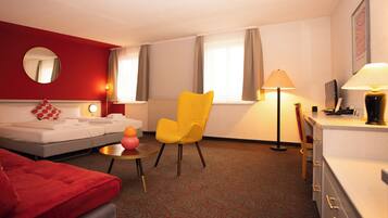 Een hotelkamer met een bed, een gele stoel, een bureau met een lamp en een rode bank.