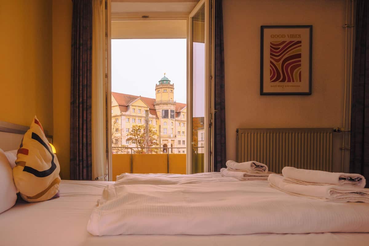 A hotel room with a bed, pillows, and a view of a building with a tower.