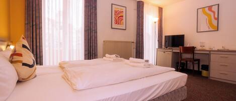 A hotel room with a bed, a desk, a chair, and a television.