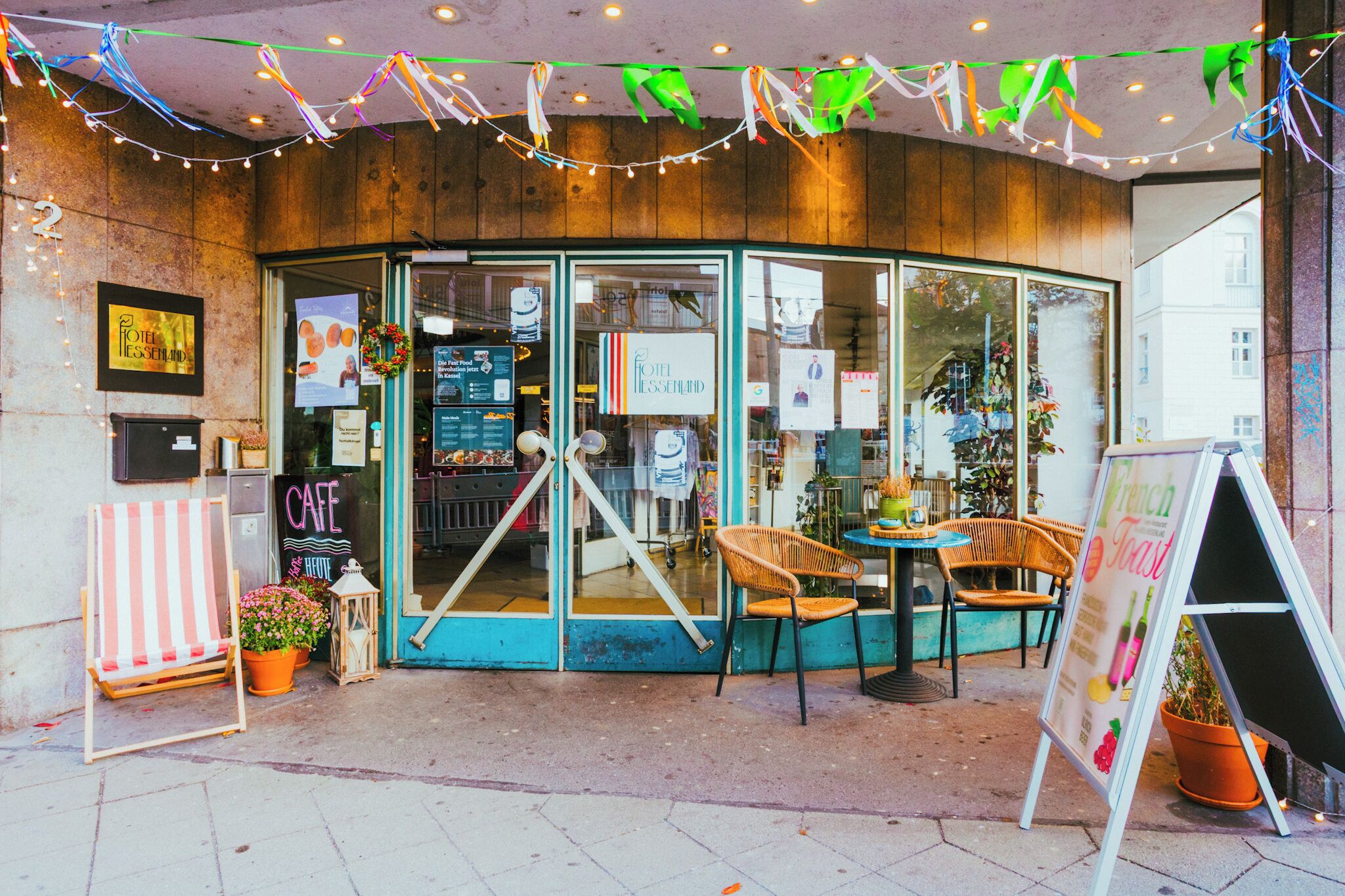 A cozy cafe with a wooden interior, a glass door entrance, and outdoor seating with wicker chairs.